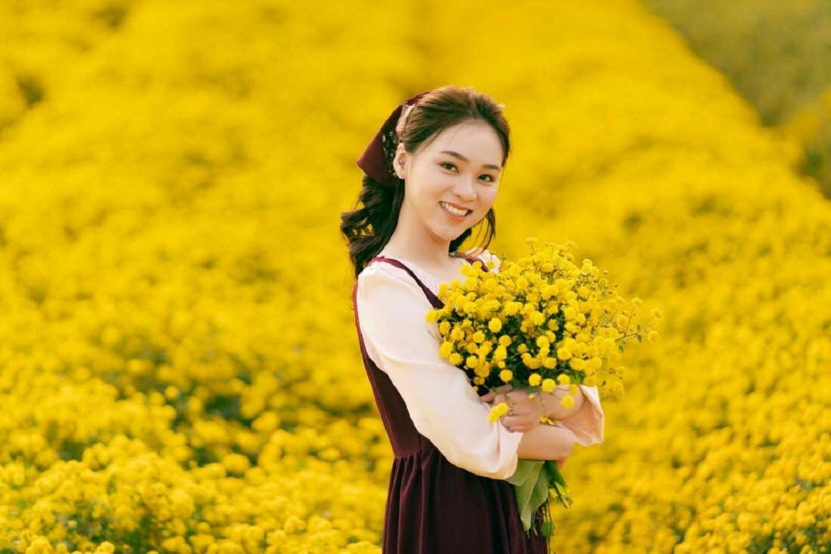 Cầm bó hoa cúc vàng trên tay 